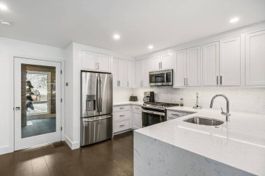 Kahverengi, ahşap zemini olan beyaz, lüks bir mutfak.