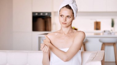 Beyaz kanepede oturan ve kendi omzuna dokunan güzel, beyaz bir bayan.