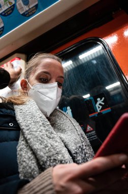 Maskeli genç kız Madrid metrosundaki cep telefonuna bakıyor.