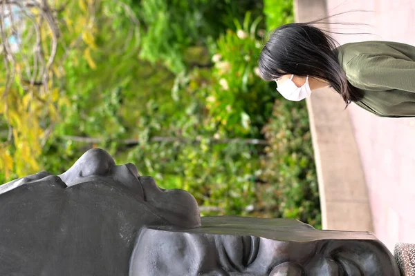 A vertical shot of a girl looking at a strange art piece in Hong Kong