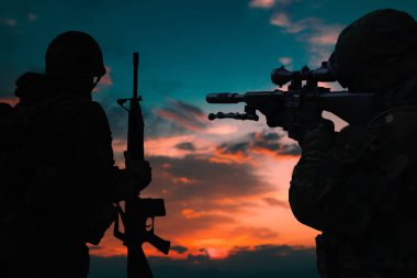 Gün batımında silahlı bir askerin silueti.