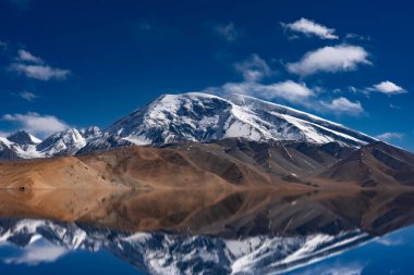 Bulutlu gökyüzüne karşı karla kaplı güzel dağların büyüleyici yansımaları.