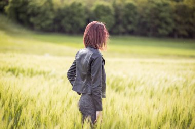 Güneşli bir günde tarlada uzun yeşil çimlerin arasında duran genç bir kadının arka plan portresi.