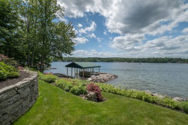 Mavi bulutlu gökyüzünün altında ağaçların olduğu parktan güzel bir göl manzarası.