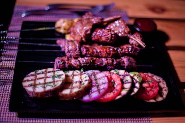 Izgara domates, patates ve soğanlı bir tabak tavuk ve biftek.