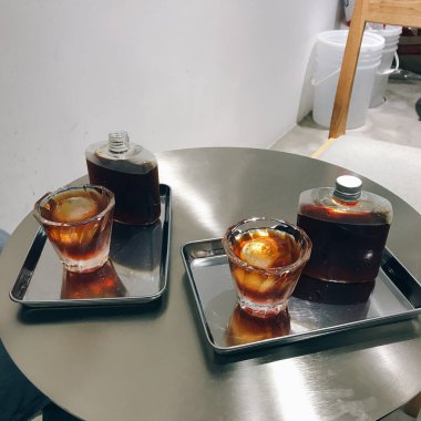 Çelik masadaki metal tepsilerin üzerine alkollü kokteyller konmuş iki bardak ve şişenin yakın çekimi.