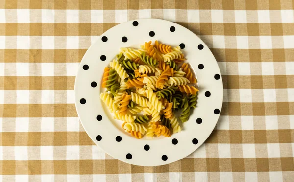 A top view of colorful rotini pasta in a plate on checkered table cloth