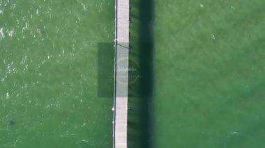 Denizde bir rıhtım manzarası ve sahilde insanlar.