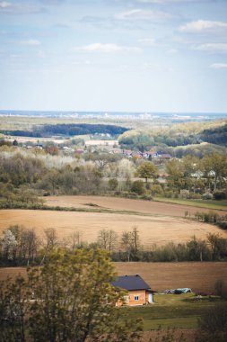 Kırsal kesimde bulutlu bir gökyüzünün altında yeşilliklerle çevrili bir kasabanın dikey görüntüsü.