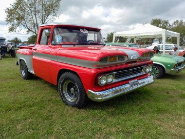Old red Chevrolet Chevy C10 Apache pickup truck 1960-1961. Green grass nature background. Utility or farming tool. Classic car show. Copyspace