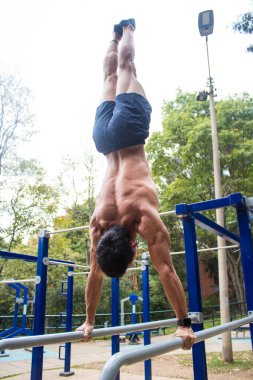 Parkta egzersiz yapan genç, üstsüz bir sporcu.