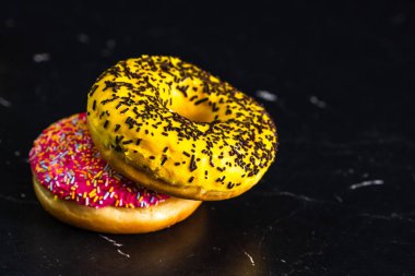 Siyah arka planda izole edilmiş sarı ve pembe jöleli çörekler