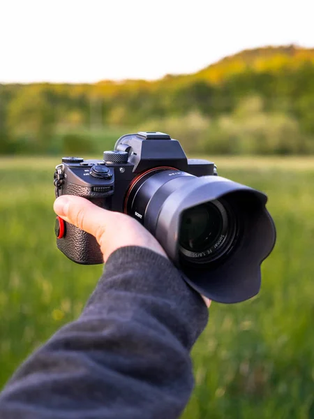 A vertical selective focus of a professional black camera in hands of a photographer in the farmland