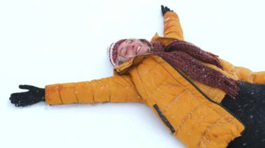 Mutlu bir genç kız beyaz kar üzerinde uzanır ve melek kanatları yapar..