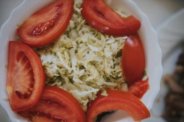 Beyaz tabakta lahana ve domatesli sebze salatası.