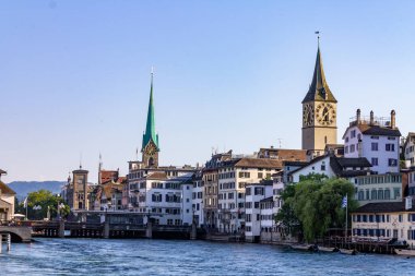 Limmat nehrinin yanındaki binalarla çevrili Fraumunster ve St. Peter kiliselerinin güzel bir manzarası.
