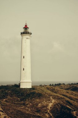 Gri bulutlu gökyüzüne karşı beyaz bir deniz fenerinin dikey görüntüsü