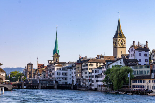 A beautiful view of Fraumunster and St Peter churches surrounded by buildings next to the Limmat river
