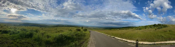 在多云的天空下 一片草地中央一条长长的沥青路面的美丽全景 — 图库照片