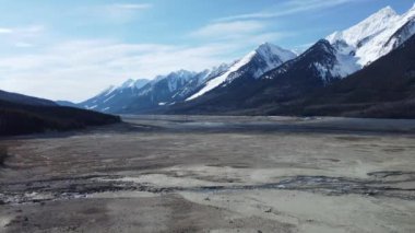 Mavi bulutlu gökyüzünün altında karla kaplı dağların olduğu bir arazinin yavaş çekim görüntüsü.