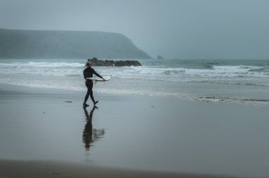Galler, Pembrokeshire 'de denize doğru giden bir erkek sörfçü.
