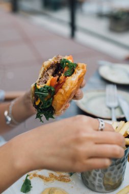 Bir elinde yarısı yenmiş hamburger tutan bir kadın diğer elinde patates kızartması yiyor.