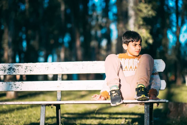 公園のベンチに足を組んで座っている怒った白人の少年 — ストック写真