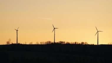 Gün batımında üç rüzgar türbini silueti. Yeşil enerji üretimi. Telefoto yavaş çekim.