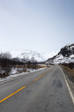 Karlı dağların arka planına karşı bir yolun dikey çekimi. Hemsedal, Norveç, Riksvei 52.