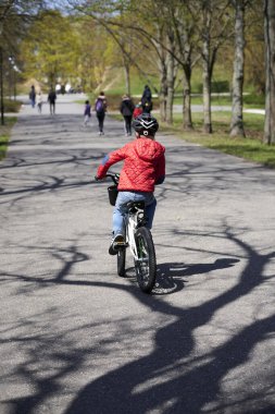 Güneşli bir bahar gününde Cytadela parkında bisiklet süren genç bir çocuk.