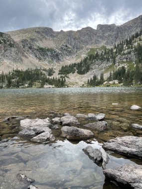 Kırsal bir alanda, ön planda gölü olan kayalık dağların dikey görüntüsü.