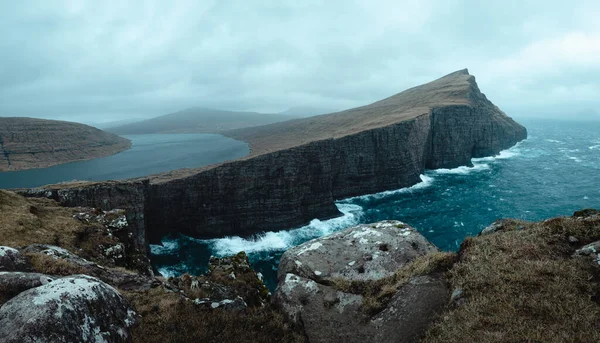 Kasvetli bir günde, Faroe Adası 'ndaki dağlı ve kayalık uçurumla denizin üzerindeki bulutlu güzel bir manzara.