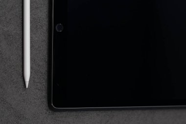 Gri kumaşta beyaz kalemle siyah ince bir tabletin üst görüntüsü.