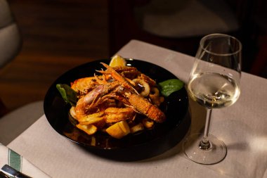 Lokantada bir bardak beyaz şarapla servis edilen kızarmış deniz ürünleri ile nefis bir yemek.