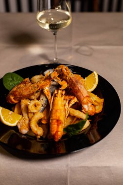 Lezzetli kavrulmuş kalamar ve portakallı karides bir bardak beyaz şarapla servis edilir.
