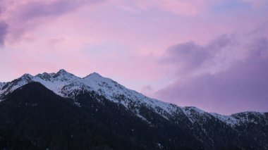 Pembe bulutlu gökyüzüne karşı karla kaplı güzel bir dağ manzarası.