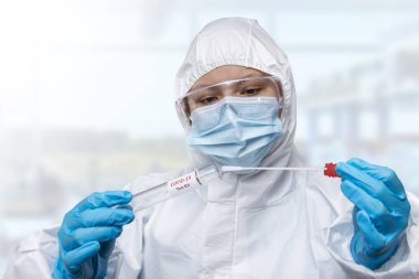 Bir NHS teknisyeni elinde COVID-19 bez toplama seti beyaz PPE koruyucu elbise ve maske takıyor.
