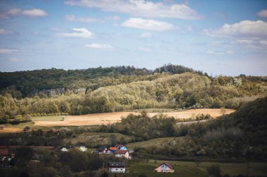 Kırsalda bulutlu bir gökyüzünün altında yeşilliklerle çevrili bir kasabanın manzarası.