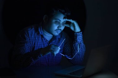 Gözlerinin altında siyah halkalı genç adam gece geç saatlerde dizüstü bilgisayarda çalışırken gözlük camını kaldırdı.