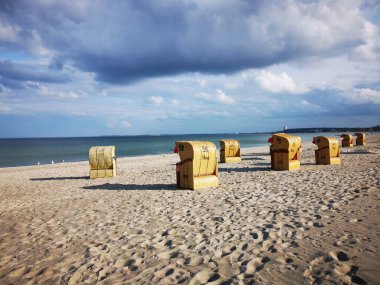 Güneşli bir günde bulutlu bir gökyüzünün altında kumlu sahildeki bankların manzarası.
