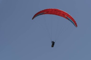 Mavi gökyüzünde kırmızı bir paraşütle uçan bir paraglider görüntüsü.