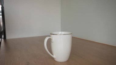 Beyaz bir fincanın üzerine çay poşetini düşüren ve ahşap bir masadan sıcak su döken bir elin yakın çekimi.