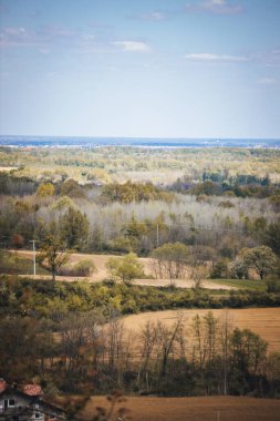 Kırsal kesimde bulutlu bir gökyüzünün altında yeşilliklerle çevrili bir kasabanın dikey görüntüsü.