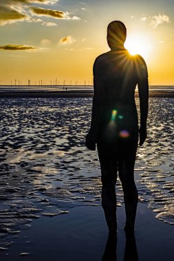 Crosby Beach, İngiltere 'de bulutlu bir günbatımında başka bir yerde bir heykelin dikey çekimi