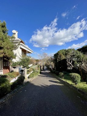 Bahçenin önündeki, bulutlu gökyüzünün altında asfalt yolu olan güzel bir lüks ev manzarası.