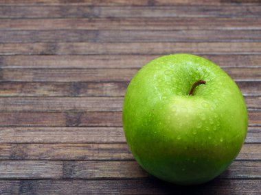 Tahta bir masanın sağ alt köşesinde, üzerinde zambak damlaları olan yeşil bir elma.