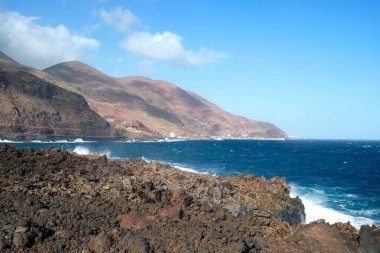 El Hierro adasının volkanik kıyıları kıyıya vuran büyük dalgalı mavi denize karşı, Puerto de la Estaca köyü, Kanarya Adaları, İspanya.