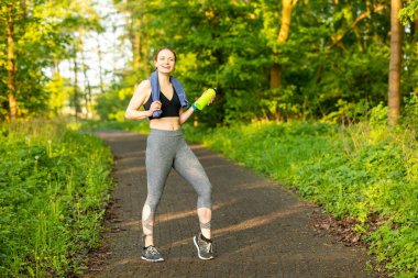 Havlu ve parkta koşmaya hazır bir şişe suyla antrenman kıyafetleri içinde genç bir beyaz kadın.