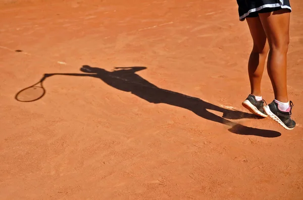 美しい晴れた日に粘土の裁判所でテニスの試合中に役立つブルネットの女の子の足と影 — ストック写真