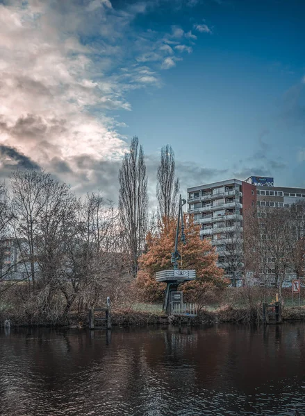 A vertical shot of a lake surrounded by autumn trees and a building on the background under cloudy sky